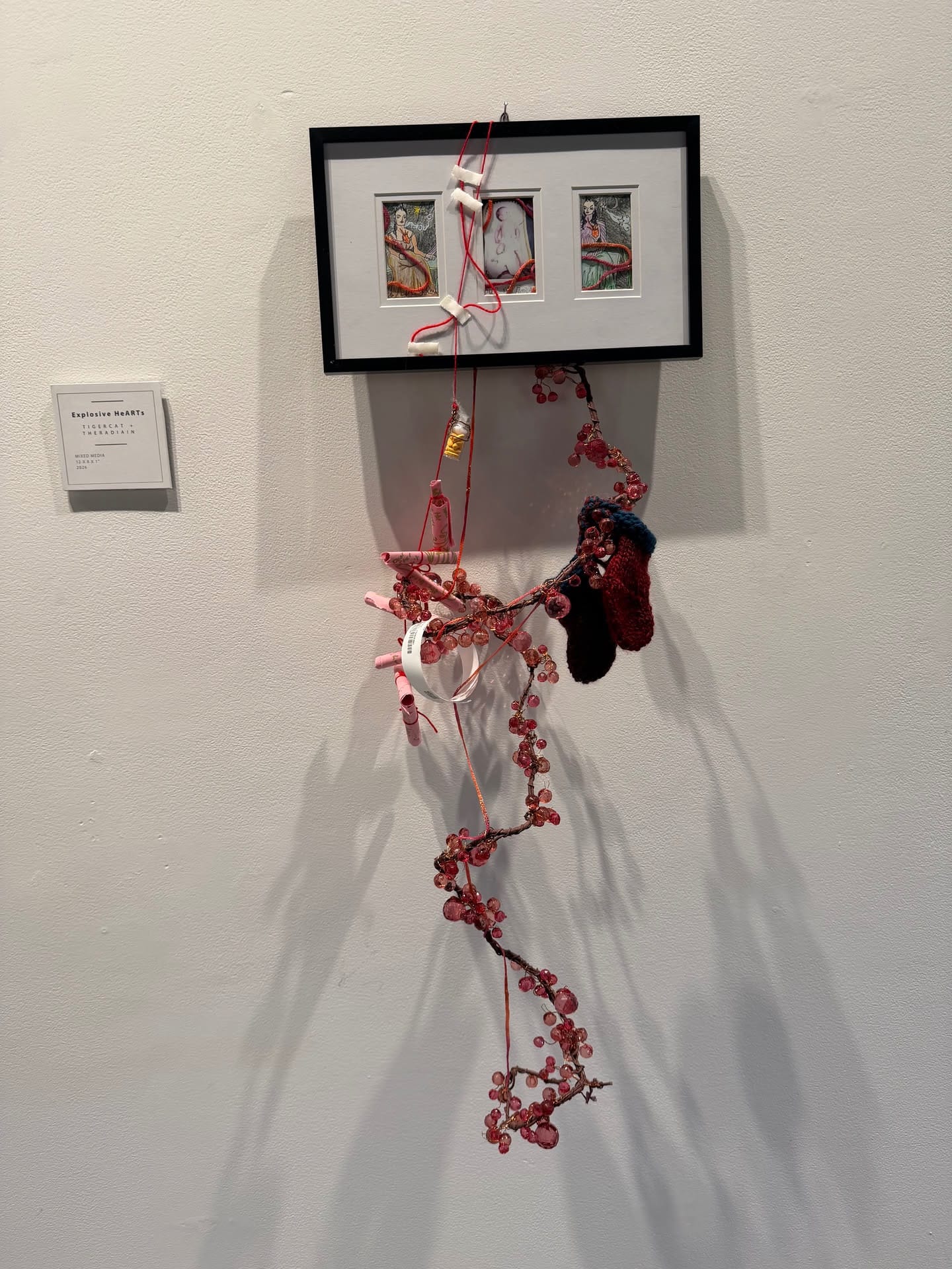 Explosive HeARTs, a framed mixed-media artwork with hanging red strands and beads