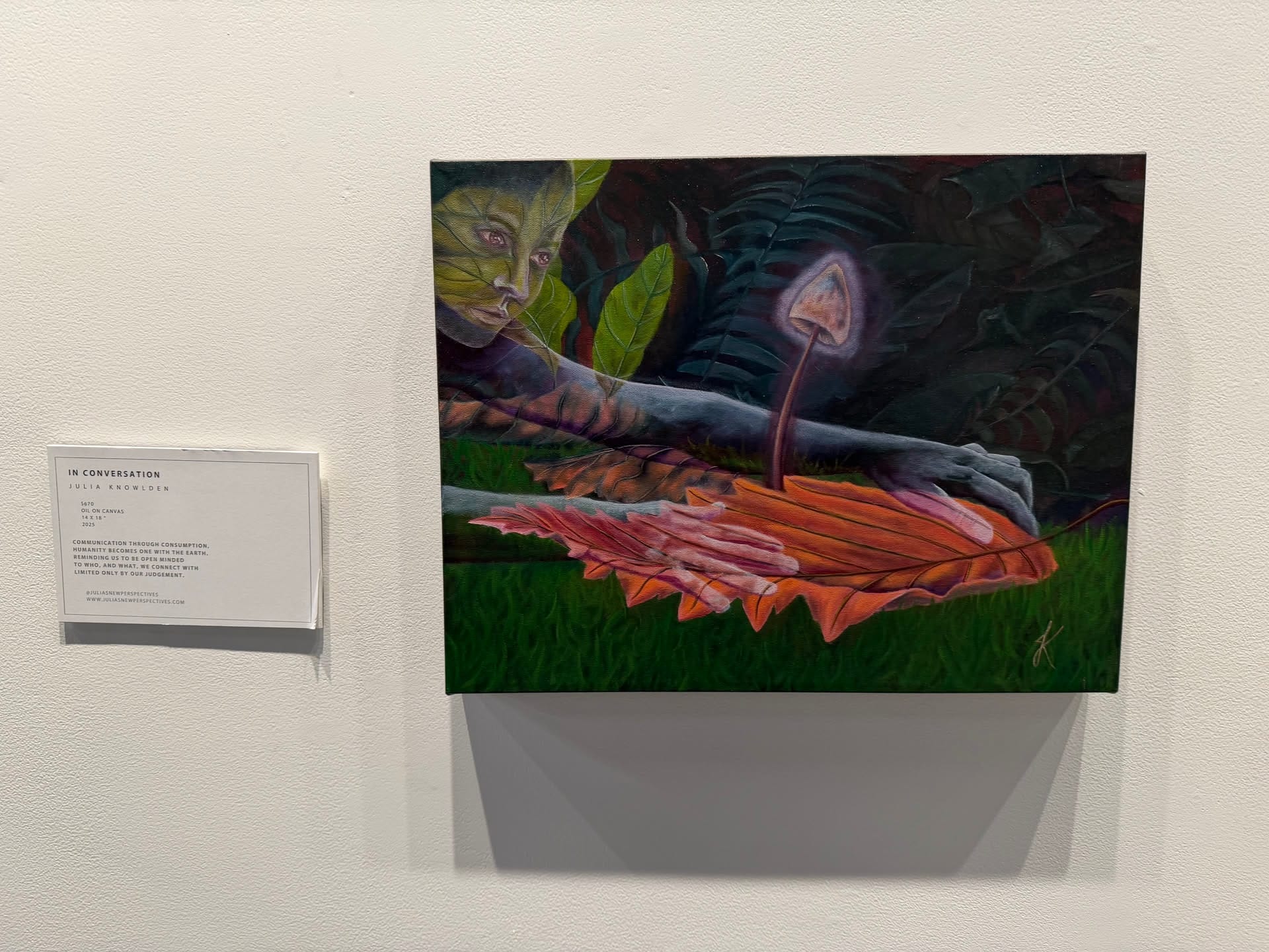 In Conversation, a painting of a figure, leaves, and a mushroom in the 2026 gallery