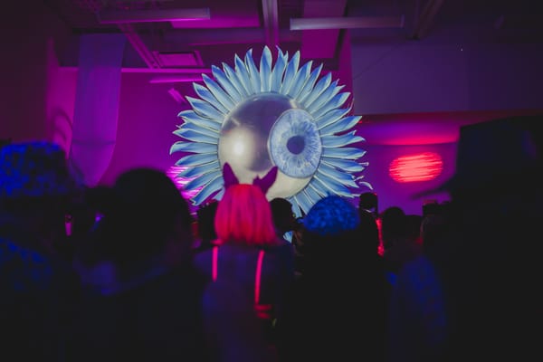 Giant gold eyeball in the centre of a huge flower gazing above the dance floor.